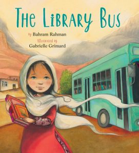 A young girl in a hijab holds books as she stands outside a teal bus.