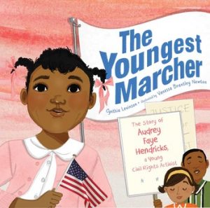 A young Black girl in pink holds a small American flag.