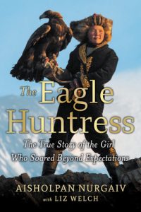 A young Mongolian girl stands on a mountain with a large eagle on her hand.