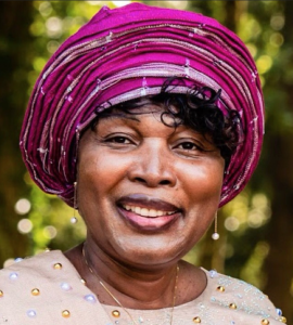 Vivian wearing a pearled top and a vivid pink headwrap. She's smiling.