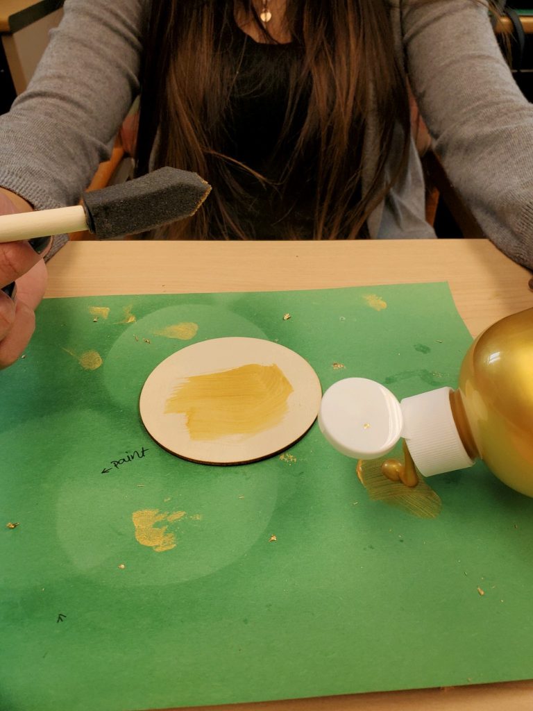 woman uses sponge brush to apply gold paint to green construction paper