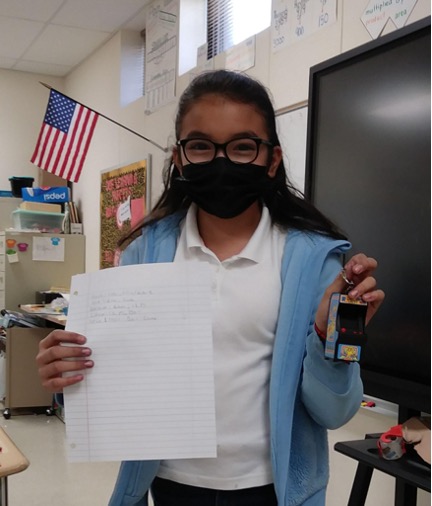 girl in medical mask holding up lined paper with writing in one hand and a key chain with the other