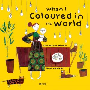 Cover art for When I Coloured in the World is a flattened illustration of a woman holding a baby in front of a dining room table with edison bulbs hanging from the top of the book, two plants and three cats filling the room.