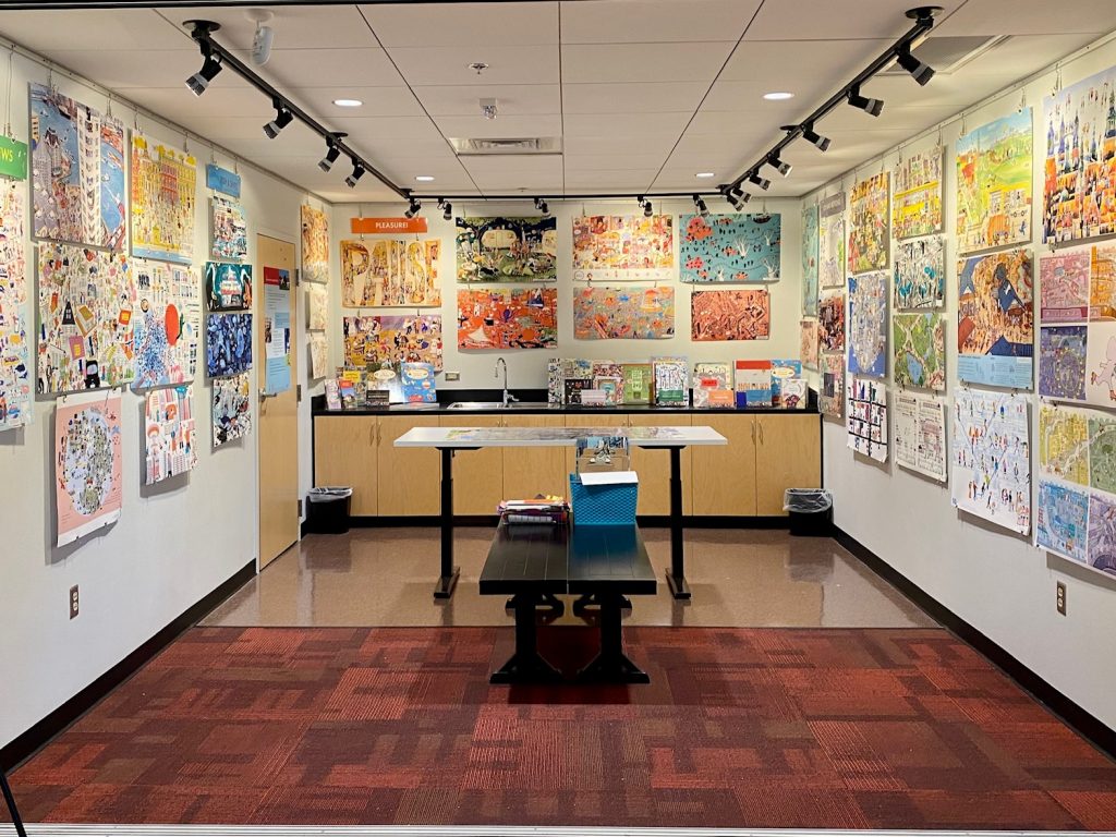 44 vibrant illustrations on the walls of a studio with books and activities set out in the center.