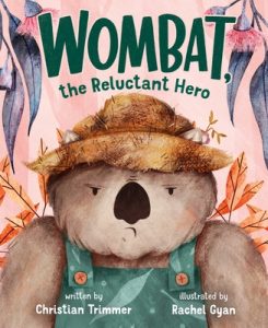 A disgruntled looking wombat in a straw hat and overalls is covered in leaves.