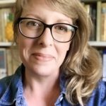 Molly Idle wearing black rimmed glasses with books behind her