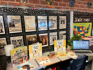 A booklist displayed on a table and against a brick wall.